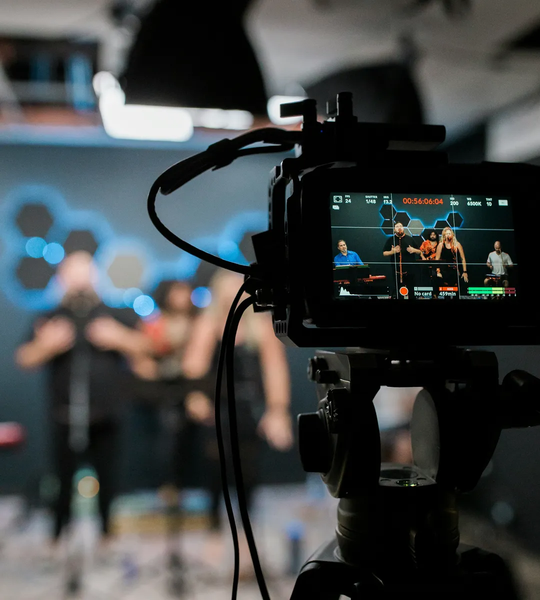 A camera on a tripod filming a live performance, the shot showing on its monitor